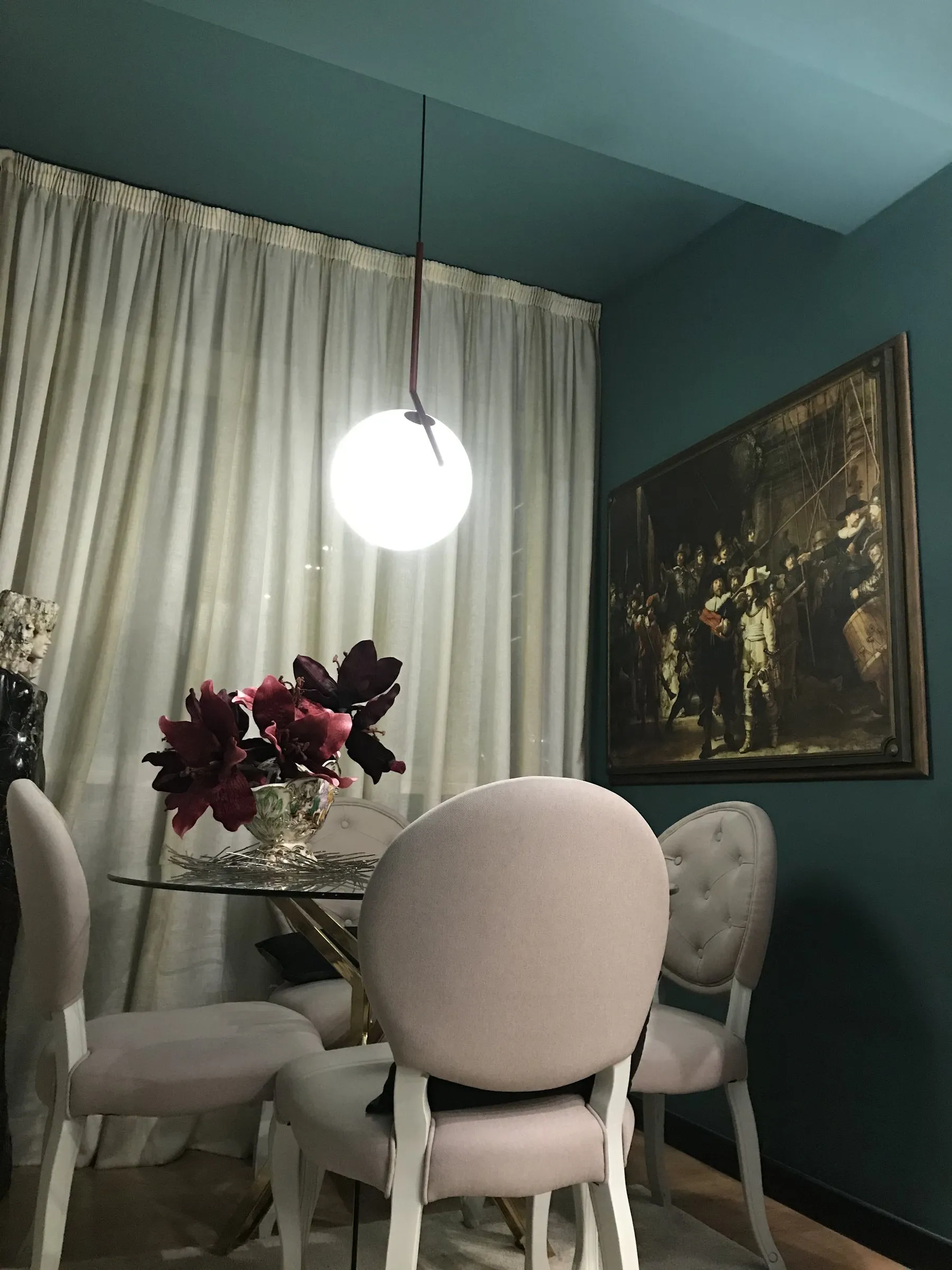 Sala de jantar com cadeiras brancas estofadas, candeeiro em globo e paredes verde-azuladas