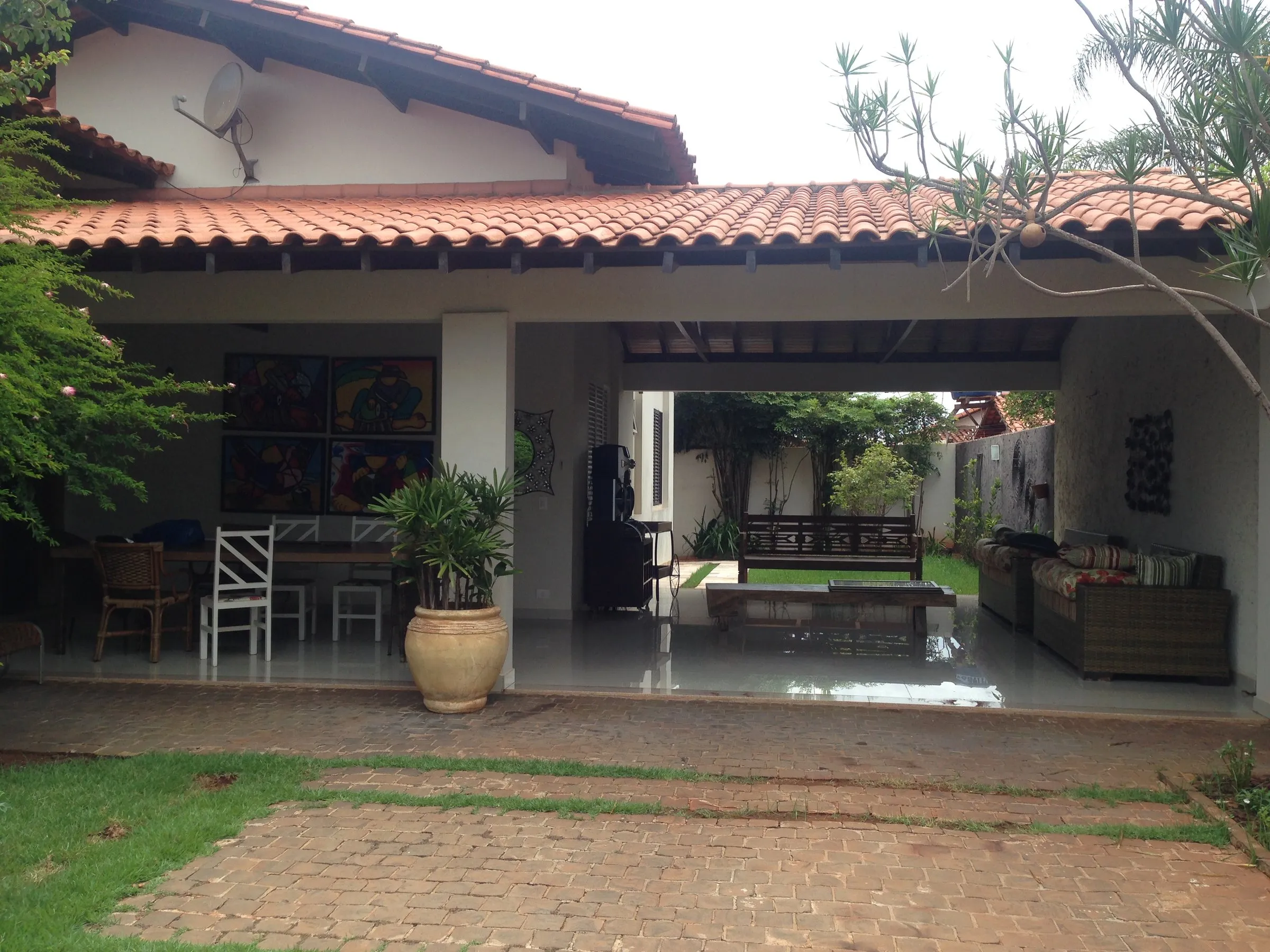 Varanda coberta com telha cerâmica aberta para o jardim, com mesa e vasos