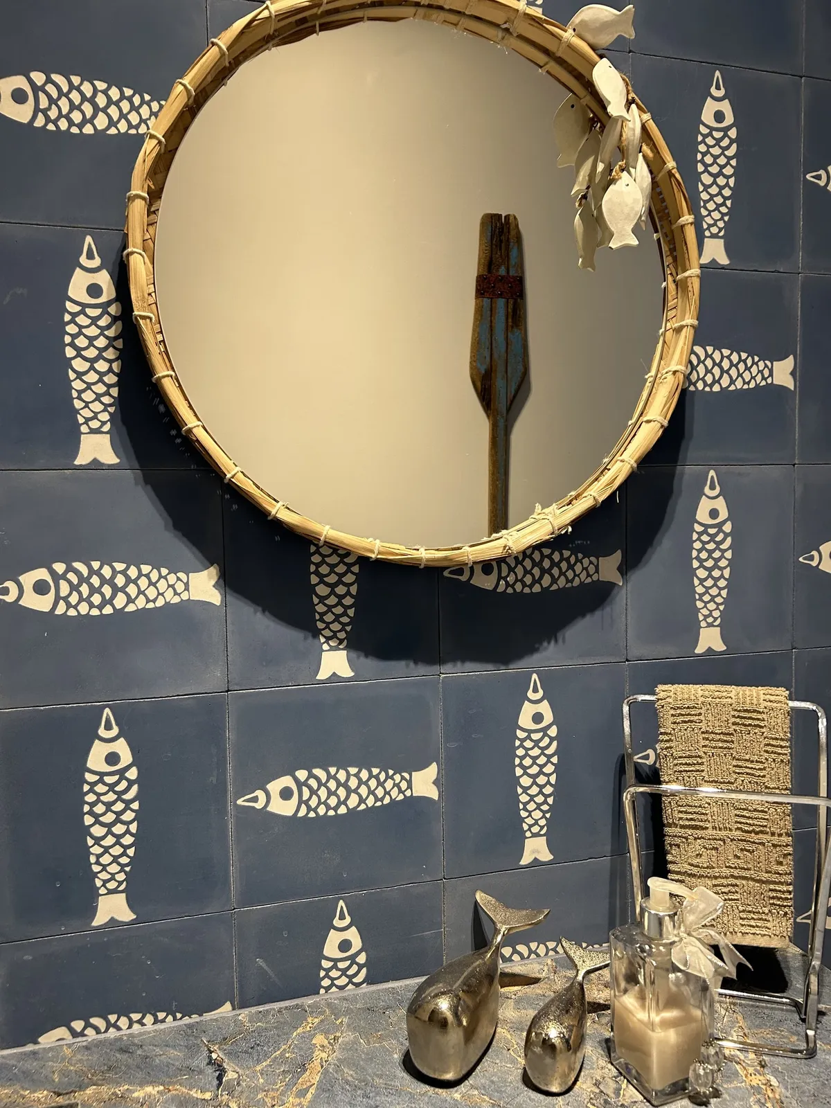 Lavabo com azulejo azul de peixes, espelho redondo com moldura de palhinha