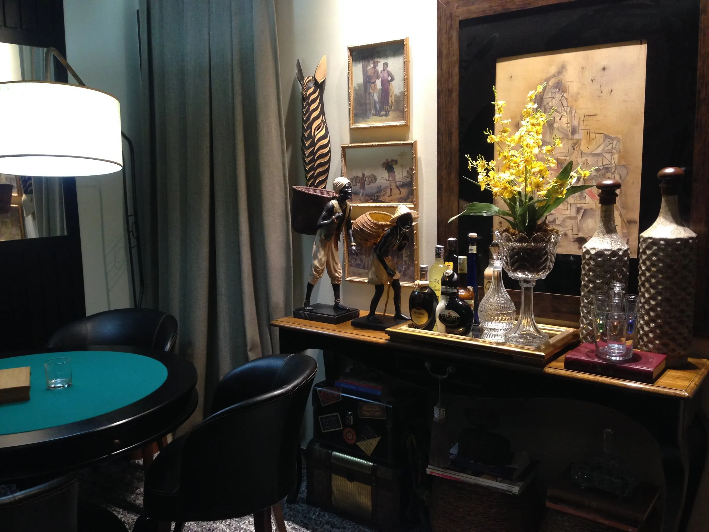 Sala de jogo com mesa de feltro verde, aparador escuro com coleção de objetos e orquídeas
