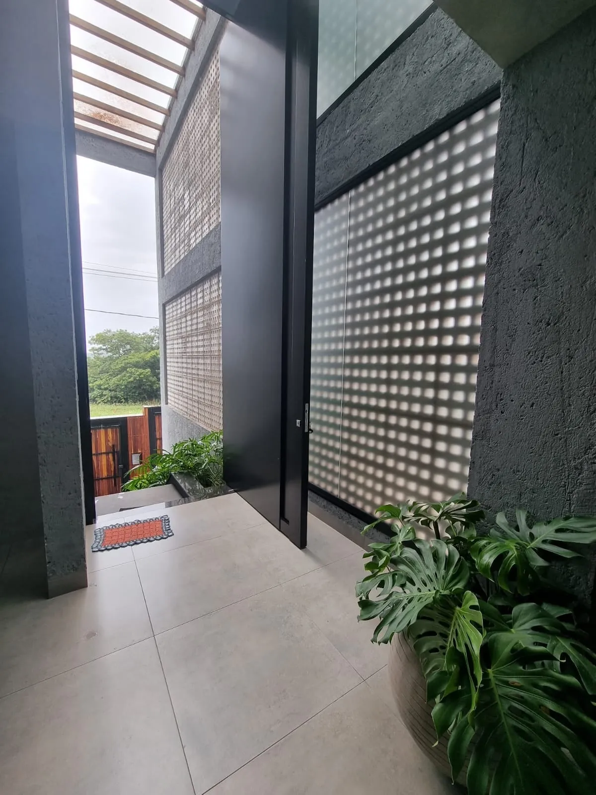 Entrada com porta pivotante preta e cobogó de betão filtrando a luz