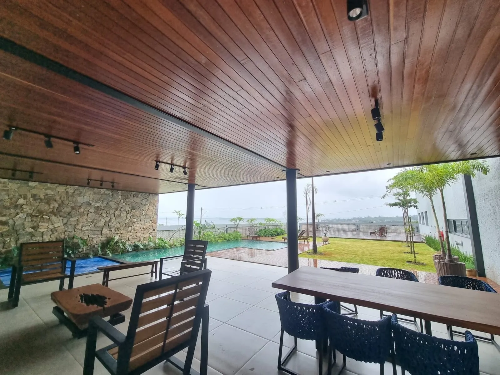 Área de lazer coberta com teto em madeira, mesa comprida e vista para o lago