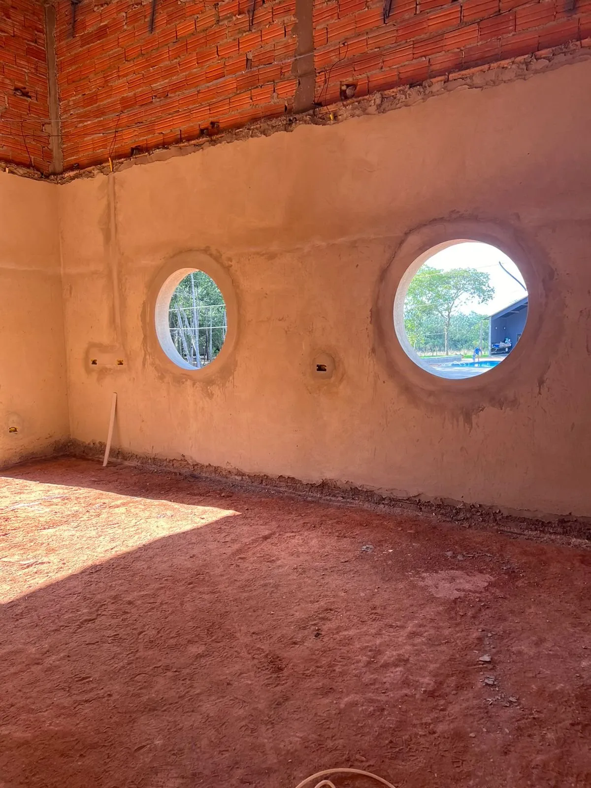 Obra em curso: parede em tosco com duas janelas redondas e chão de terra vermelha