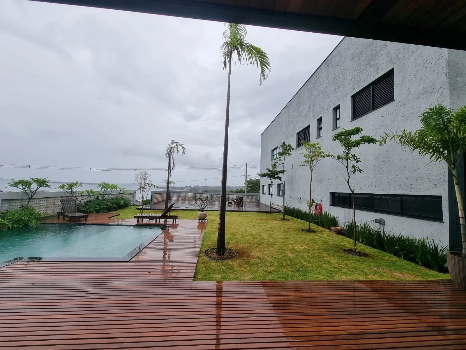 Deck de madeira, piscina e relvado junto à fachada cinzenta da casa
